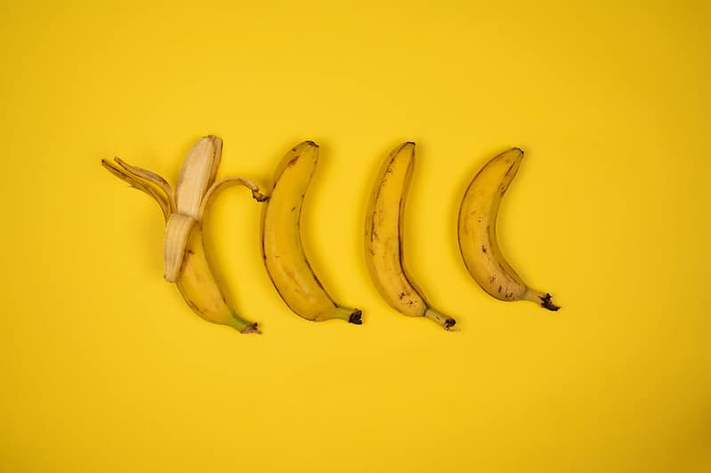 tasty fresh bananas with peel on yellow background
